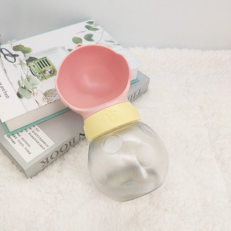 Portable dog water bottle with pink bowl and transparent container on a table.