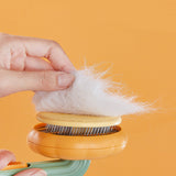 Hand holding pet cat brush with collected white fur on a yellow background.