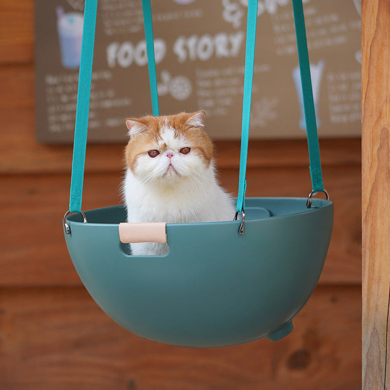 Cat sitting in a moss green hanging pet nest bed.